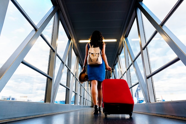 Viajero de la chica joven que camina con llevar la maleta del asimiento en el aeropuerto. Concepto turístico.