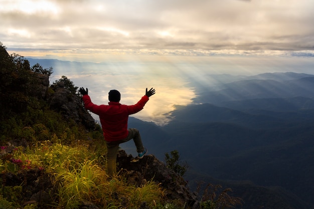 Un viajero en la cima de la montaña, él parado en la roca viendo un amanecer