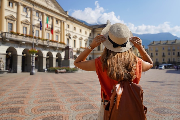 Viajero elegante mujer sostiene sombrero en un día soleado en la ciudad de Aosta, Italia