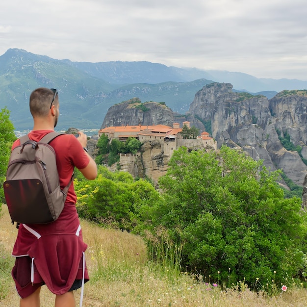 El viajero está tomando una foto con un teléfono celular parado en la cima de la montaña. El turista está tomando una foto con la cámara el día de verano en el valle de Meteora.