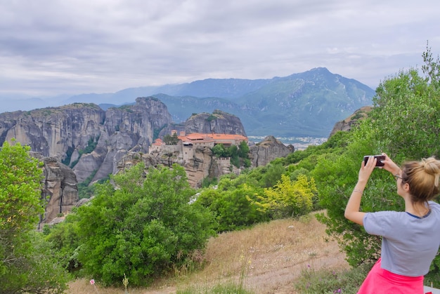 El viajero está tomando una foto con un teléfono celular parado en la cima de la montaña. El turista está tomando una foto con la cámara el día de verano en el valle de Meteora.