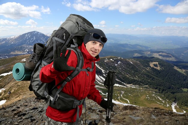 El viajero feliz equipado con una chaqueta roja en la ladera levantada en la mano de saludo