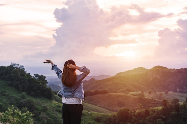 Viajero feliz joven relajante y mirando la hermosa puesta de sol en la cima de la montaña