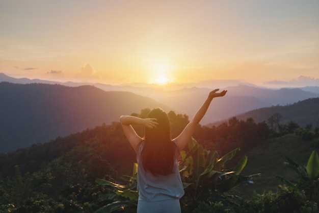 Foto viajero feliz joven relajante y mirando la hermosa puesta de sol en la cima de la montaña