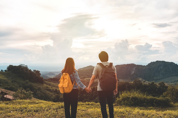 Viajero feliz pareja joven relajante y mirando la hermosa puesta de sol en la cima de la montaña