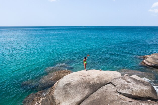 Viajero femenino se para sobre una roca y admira el mar azul