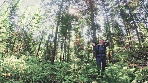 Viajero fotografiando vistas panorámicas en el bosque Una mujer caucásica disparando una bonita mirada mágica Chica toma un video fotográfico en una cámara sin espejo dslr Fotógrafo profesional de viaje con mochila al aire libre