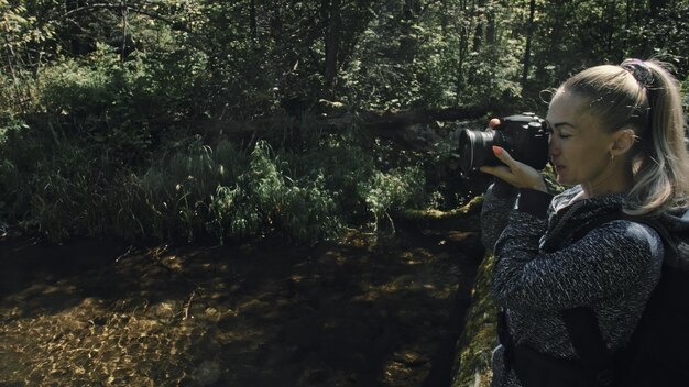 Foto viajero fotografiando vistas panorámicas en el río del bosque puente de madera árbol caído una mujer caucásica disparando una bonita mirada mágica chica toma una foto en la cámara