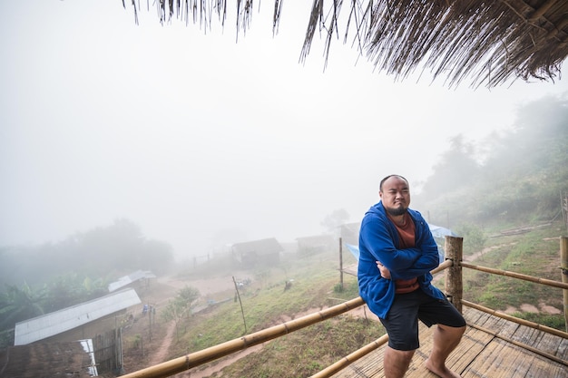 Viajero gordo asiático sentado en el balcón de madera con hermosos paisajes y niebla en la mañana de Sapan Village nan ThailandSapan es un pueblo pequeño y tranquilo en la montaña