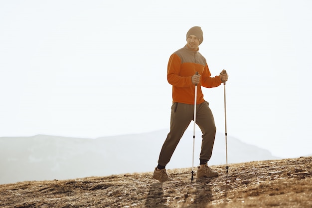 Viajero hombre con bastones de trekking subiendo la montaña