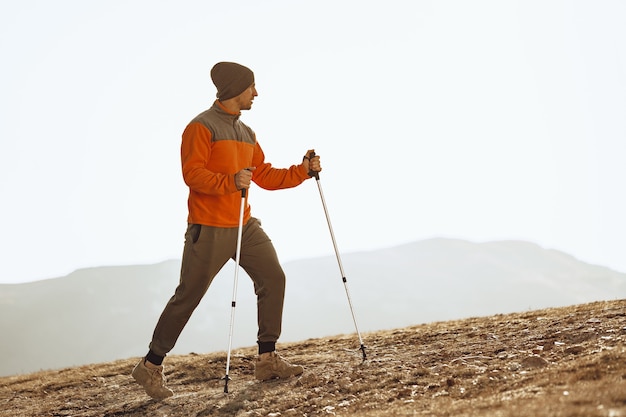 Viajero hombre en ropa deportiva con palos de trekking subiendo la montaña