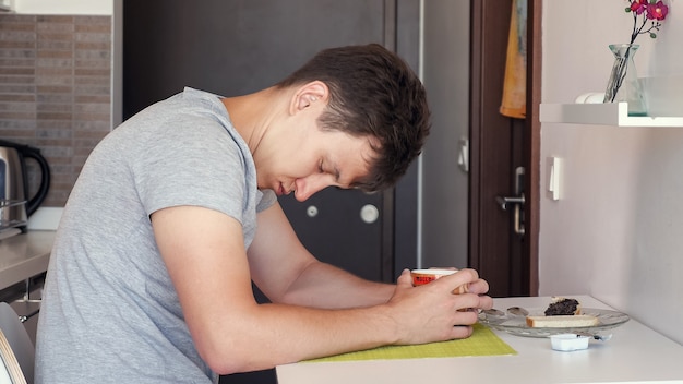 Viajero hombre con una taza de té sentado y dormido en la pequeña cocina, vista lateral