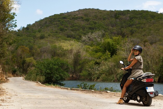 Viajero joven está conduciendo scooter en el antiguo camino rural en las montañas