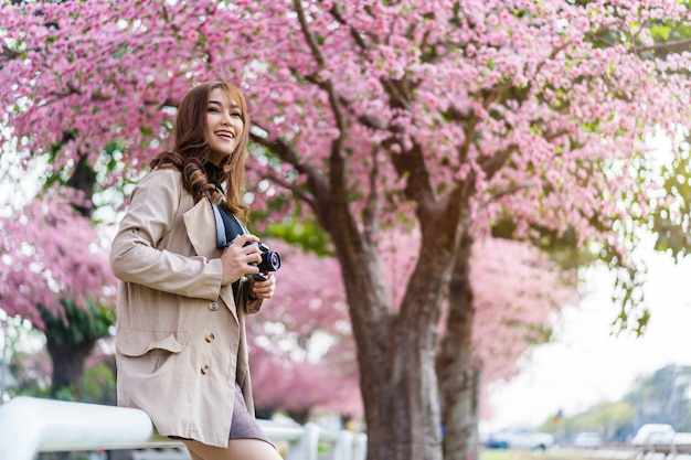 Viajero joven mirando flores de cerezo o flor de sakura floreciendo y sosteniendo la cámara para tomar una foto en el parque