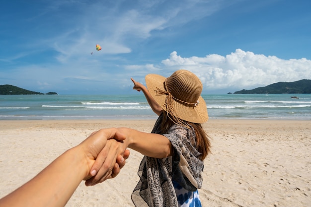 Viajero joven que sostiene la mano del hombre y que mira el vuelo del paracaídas en el cielo en la playa