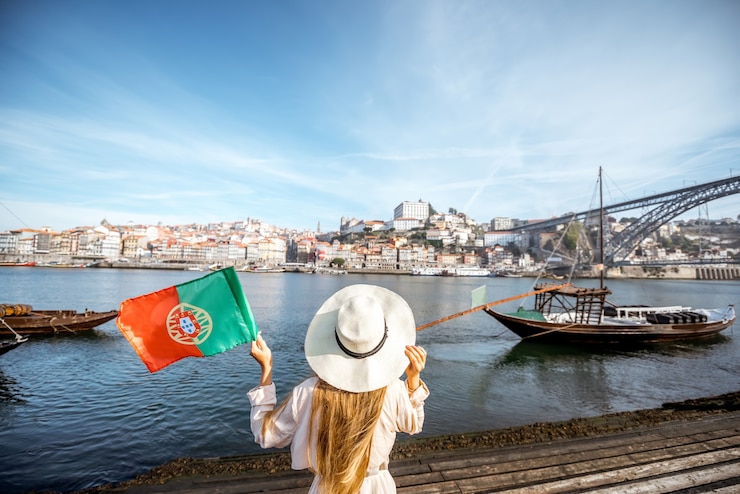 Foto viajero joven retrocediendo con bandera portuguesa, disfrutando de la hermosa vista del paisaje urbano sobre el río duero y los barcos durante la luz de la mañana en oporto, portugal