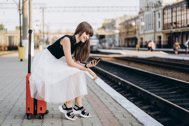 Viajero con maleta roja esperando tren en la estación de tren