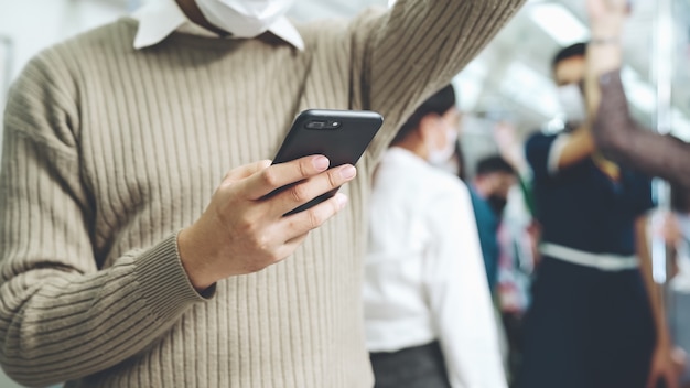 Viajero con mascarilla mientras usa el teléfono móvil en el tren público