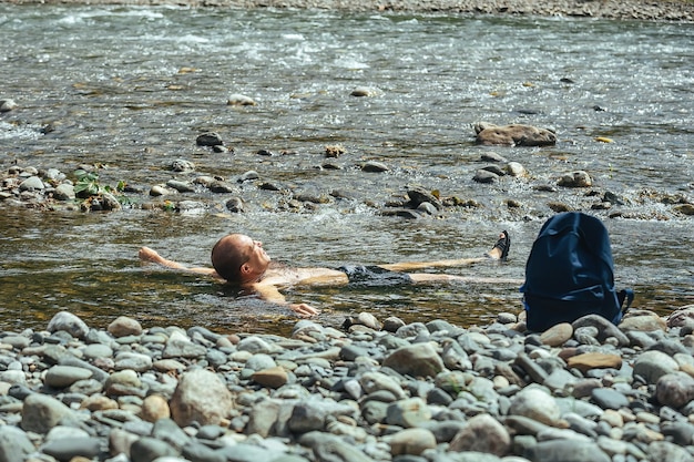 Viajero masculino se baña en un río de montaña con agua fría y clara mientras camina por las montañas