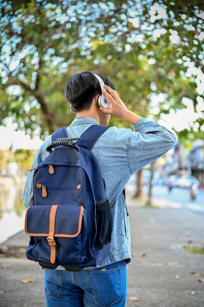 viajero masculino escuchando música a través de sus auriculares mientras pasea por la vista trasera de la ciudad