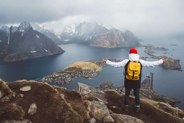 Viajero con una mochila amarilla de pie sobre las rocas con el telón de fondo del mar y las montañas. Espacio para su mensaje de texto o contenido promocional. Concepto de estilo de vida de viaje.