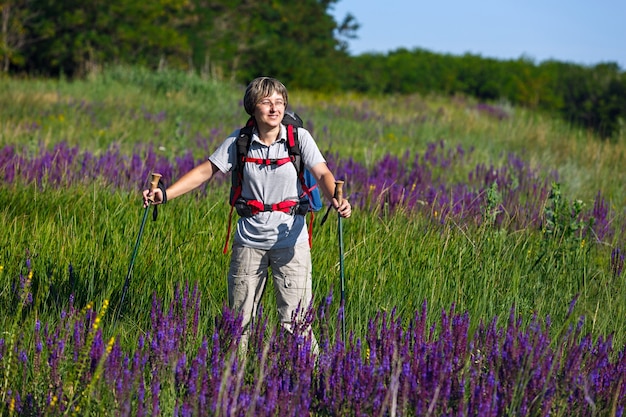 Viajero con mochila y bastones de senderismo. La niña es una viajera en el prado con flores. Fotografiado en Rusia.