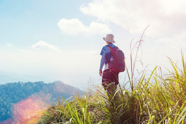 Viajero con mochila de pie y mirando hacia la cima de la montaña con luz solar