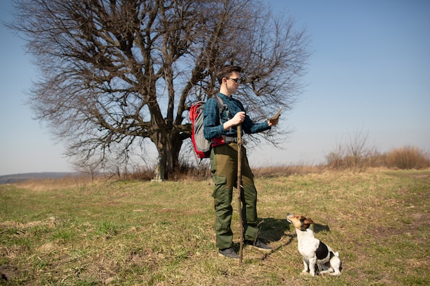 Un viajero con una mochila y su perro, mirando el mapa y caminando por el campo.