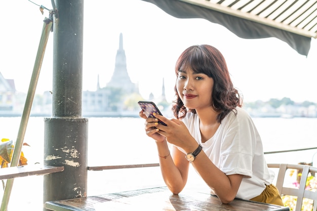 Viajero mujer asiática usando su teléfono en la cafetería