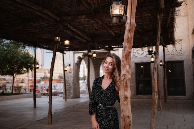 Viajero mujer feliz con vestido negro caminando por las calles de una antigua ciudad o aldea árabe en medio del desierto. Lámparas de aceite árabe tradicional en la calle Al Seef Dubai