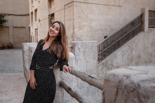 Viajero mujer feliz con vestido negro caminando por las calles de una antigua ciudad o aldea árabe en medio del desierto.