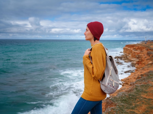 Viajero de mujer hipster en suéter amarillo y sombrero rojo disfrutando del aire fresco