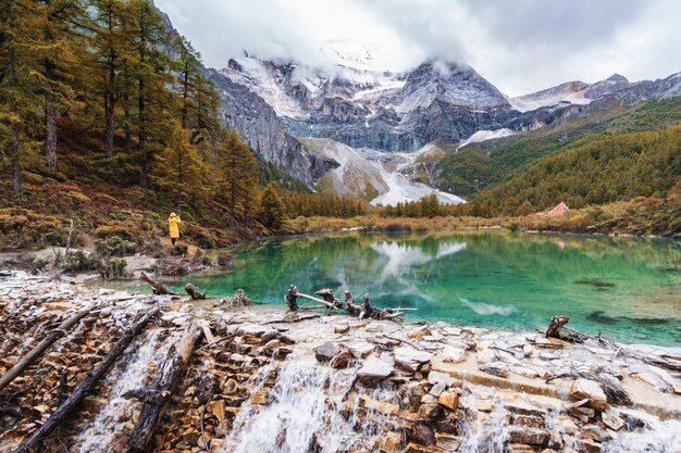 Viajero de la mujer joven que camina y que fotografía paisaje hermoso en la reserva de naturaleza de Yading, concepto de la forma de vida del viaje