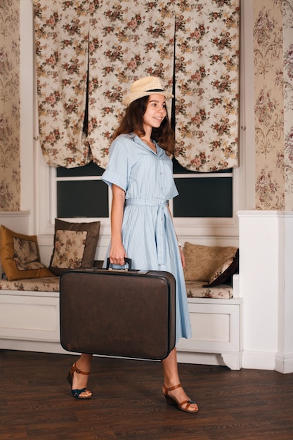 Viajero mujer joven con sombrero blanco caminando en la habitación con equipaje.