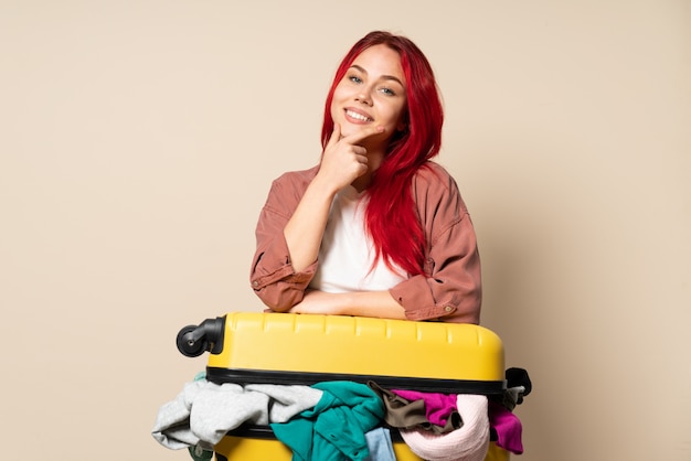 Viajero mujer con una maleta llena de ropa aislado en la pared de color beige feliz y sonriente