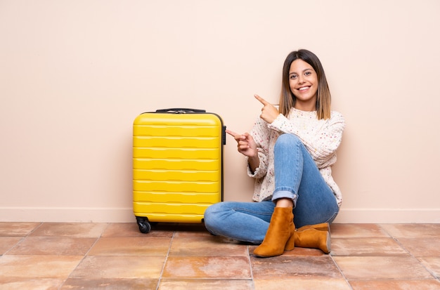 Viajero mujer con maleta sentada en el suelo apuntando con el dedo a un lado