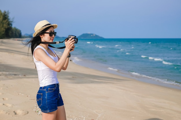 Foto viajero mujer de pie en la playa y tomar fotos para ver el mar de vacaciones.
