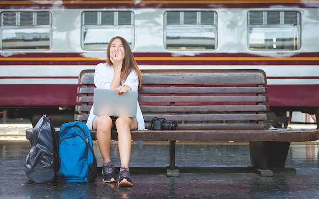 Viajero mujer sentada sola y riendo con la computadora portátil y el bolso.