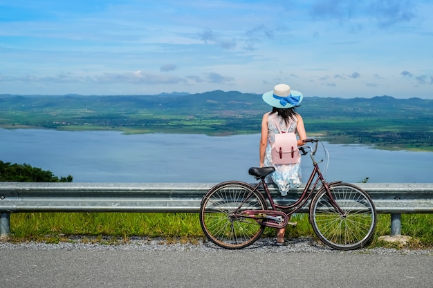 Viajero de mujer sentado cerca de una bicicleta y tomando foto vista de la presa