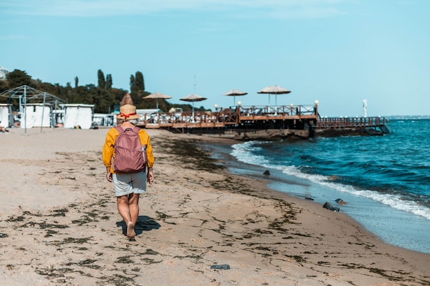 Viajero de mujer con un sombrero de verano y turista en mochila camina en la playa