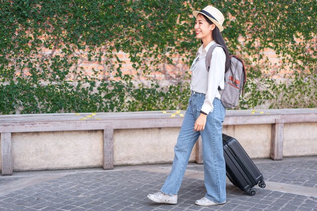 Viajero de mujer sonriente arrastrando la bolsa de equipaje maleta negra caminando al embarque de pasajeros en el aeropuerto, concepto de viaje.