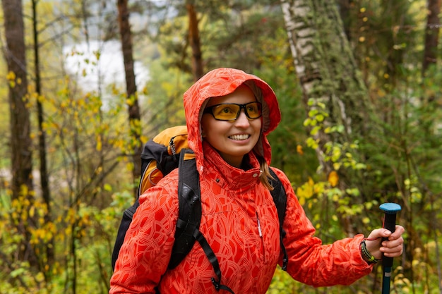 Viajero de mujer sonriente con una mochila camina por el bosque de otoño en tiempo lluvioso