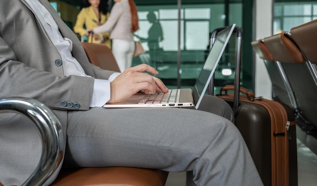 Viajero de negocios usando una computadora portátil mientras está sentado en la zona de espera del aeropuerto