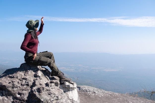 Un viajero se sienta en una roca en una montaña alta con una hermosa vista del cielo