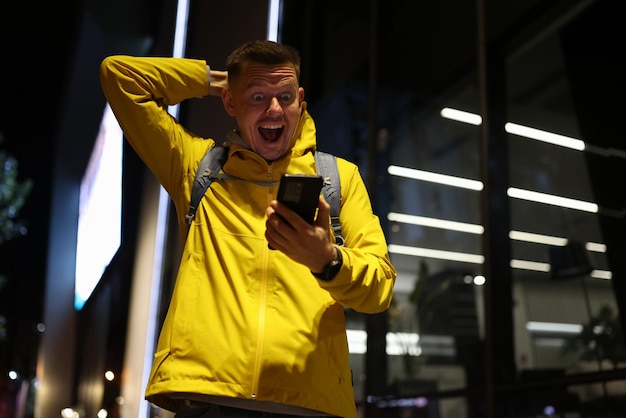 Viajero sorprendido con la boca abierta mirando la pantalla del teléfono inteligente en la calle