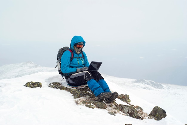 Viajero trabajando con un portátil en invierno en la cima de una montaña durante las nevadas