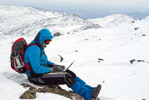 Viajero trabajando con un portátil en invierno en la cima de una montaña durante las nevadas