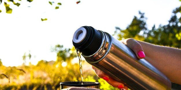 Viajero vertiendo té caliente del termo a la taza en otoño bosque caído al aire libre. Picnic de otoño de verano. Copia espacio