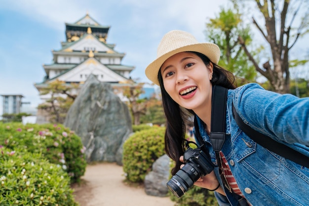 viajero visitando el castillo de osaka solo y tomando selfie. joven fotógrafo asiático sosteniendo una cámara digital y autorretrato con el castillo de osaka parado en el jardín verde. Vacaciones de viaje de Asia en Japón