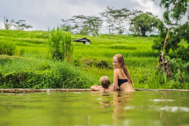 Viajeros de mamá e hijo en Belulang Hot Springs en Bali al fondo de las terrazas de arroz. Concepto de viajar con niños